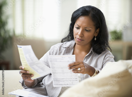 Photo: Hispanic woman sitting on sofa reading bills Hispanic woman sitting on sofa reading bills