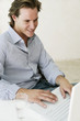 Photo: Young male looking content whilst working on laptop at home Young male looking content whilst working on laptop at home