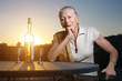 Elderly woman sitting at the table outdoors at sunset.