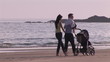 Happy couple walking on the beach with their baby on a stroller
