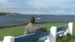 Rear view of a man looking the bay sitting on a bench