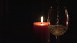 Candle with glass of white wine in the foreground in the dark
