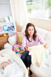 Joyful young mom holding a baby pyjamas sitting on sofa