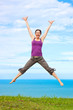 Beautiful young woman jumping and laughing by the ocean
