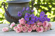 Purple aster and pink roses with a antique vase on a wooden tabl Purple aster and pink roses with a antique vase on a wooden tabl