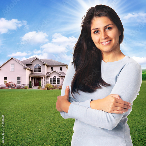 Photo: Young woman standing in front of house smiling Young woman standing in front of house smiling