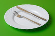 White dinner plate, knife, and fork on a green background