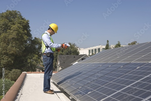 Photo: Maintenance worker stands with solar array on rooftop, Los Angeles, California Maintenance worker stands with solar array on rooftop, Los Angeles, California