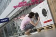 Young woman looks inside tub of washing machine in shopping mall, Voronezh