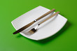 White square plate, knife, and fork on green background