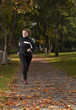 Beautiful female athlete running in park on autumn day.