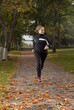 Beautiful female athlete running in park on autumn day.