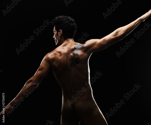 Naked young man with tattoo on his back against black background