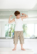 Funny little kid standing on kiitchen and looking at his muscles