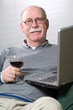 Senior man working on laptop with a glass of wine