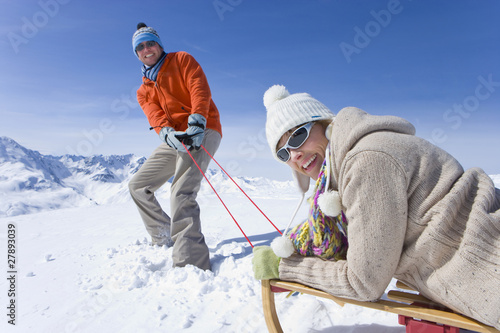 Photo: Man puling wife through snow on sled Man puling wife through snow on sled