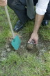 Hand with shovel hiding jar of coins in grass