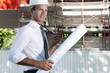 Man with hardhat, walky talky radio, and architectural plans at construction site