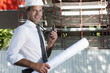 Man with hardhat, walky talky radio, and architectural plans at construction site