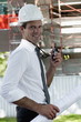 Man with hardhat, walky talky radio, and architectural plans at construction site