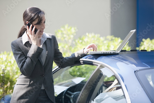 Foto: Businesswoman next to car with laptop talking on smartphone Businesswoman next to car with laptop talking on smartphone