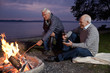 Two senior men sitting beside a campfire drinking wine
