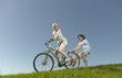 A woman on a bicycle, man holding onto the back