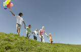 Photo: A family walking through the grass holding hands, father holding a bunch of colorful balloons A family walking through the grass holding hands, father holding a bunch of colorful balloons