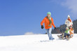 Father pulling children on sled downhill on ski slope