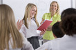 School girl reading out of test booklet in classroom to classmates