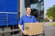 Truck driver standing near semi-truck holding cardboard box