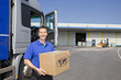 Truck driver standing near semi-truck on loading dock holding cardboard box