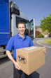 Truck driver standing near semi-truck holding cardboard box
