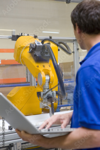 Photo: Worker watching robotic arm working on assembly line in factory Worker watching robotic arm working on assembly line in factory