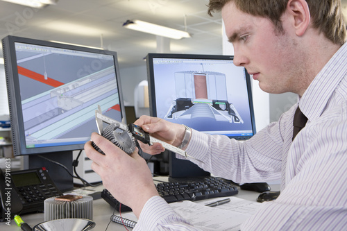 Photo: CAD designer measuring part at desk in office CAD designer measuring part at desk in office