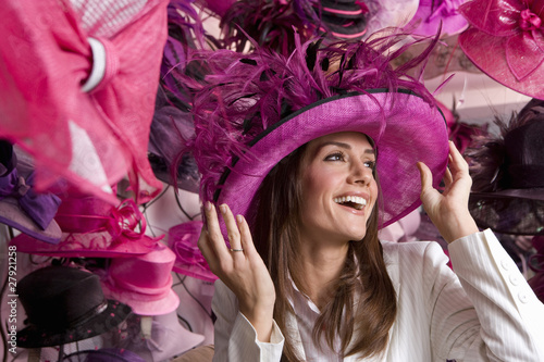 Foto: Customer trying on ornate pink feathered hat in shop Customer trying on ornate pink feathered hat in shop