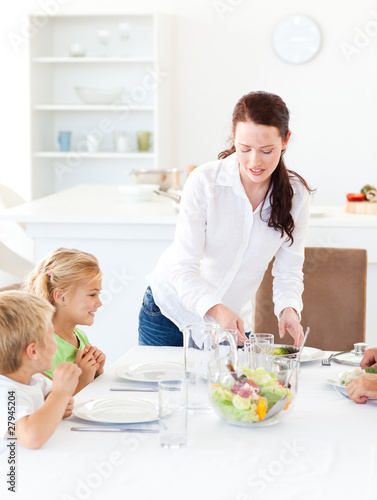 Photo: Adorable mother serving salad to her children for lunch Adorable mother serving salad to her children for lunch
