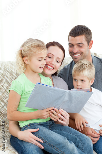 Photo: Adorable family reading a book together in the living-room Adorable family reading a book together in the living-room