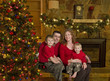 Family of four sits beside christmas tree Family of four sits beside christmas tree