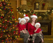 Family of four with santa hats sits beside christmas tree Family of four with santa hats sits beside christmas tree