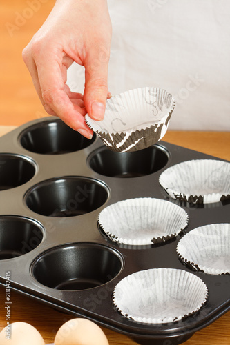 Photo: A female cook 's hand putting muffin cups in the oven pan. A female cook 's hand putting muffin cups in the oven pan.