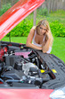 Young beautiful woman standing near red car and looking under ho