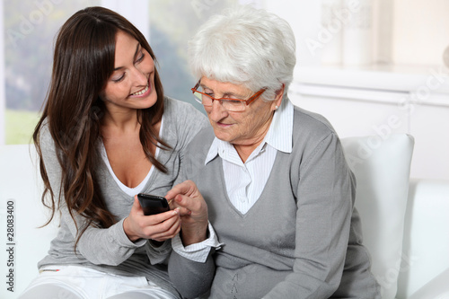 Photo: Young woman showing how to use mobile phone to grandmother Young woman showing how to use mobile phone to grandmother