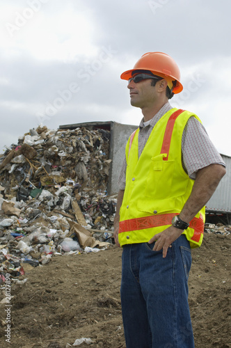 Photo: Worker standing near truck dumping waste at landfill site Worker standing near truck dumping waste at landfill site