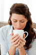 Pretty woman smelling her coffee on the sofa at home