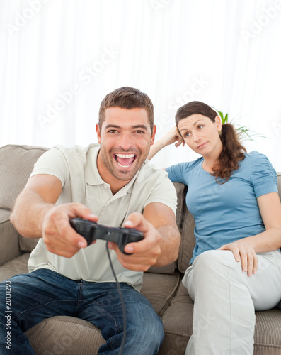 Photo: Bored woman looking at her boyfriend playing video game on the s Bored woman looking at her boyfriend playing video game on the s