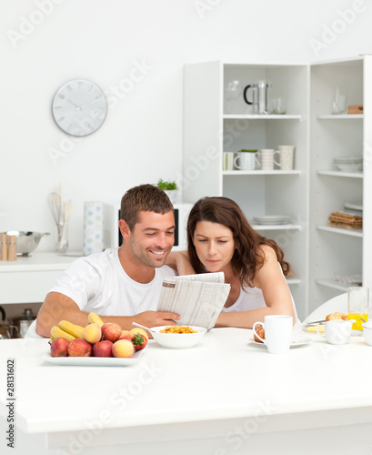 Photo: Happy couple reading the newspaper in the kitchen Happy couple reading the newspaper in the kitchen
