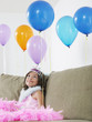 Foto: Young girl 7-9 sitting on sofa looking at balloons Young girl 7-9 sitting on sofa looking at balloons