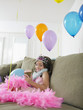 Foto: Young girl 7-9 sitting on sofa with balloons, eating cupcake Young girl 7-9 sitting on sofa with balloons, eating cupcake