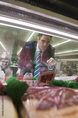 Photo: Mature man looks through glass of meat counter in supermarket Mature man looks through glass of meat counter in supermarket